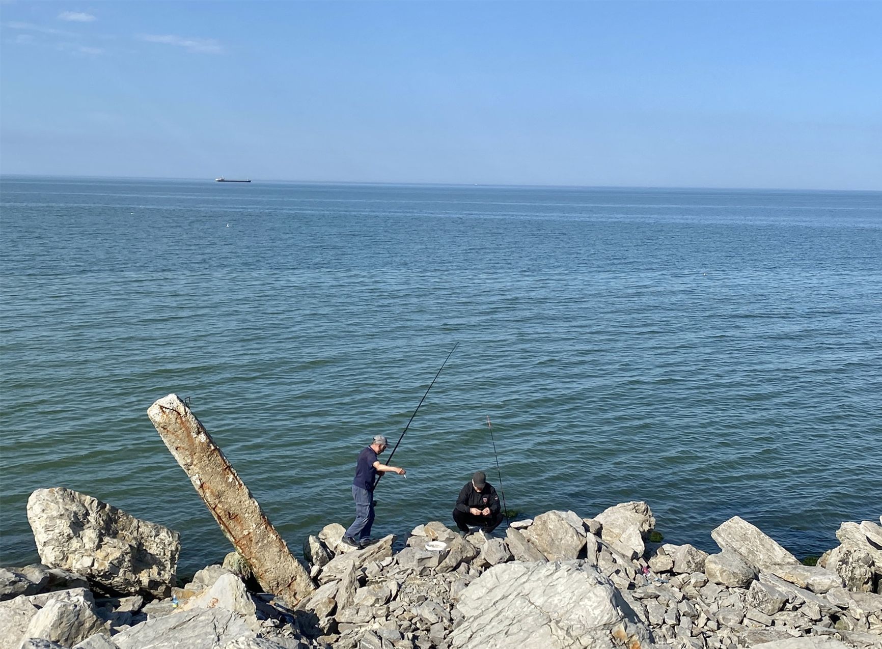 Fishermen on the rocks in Makhachkala, with a tanker on the horizon